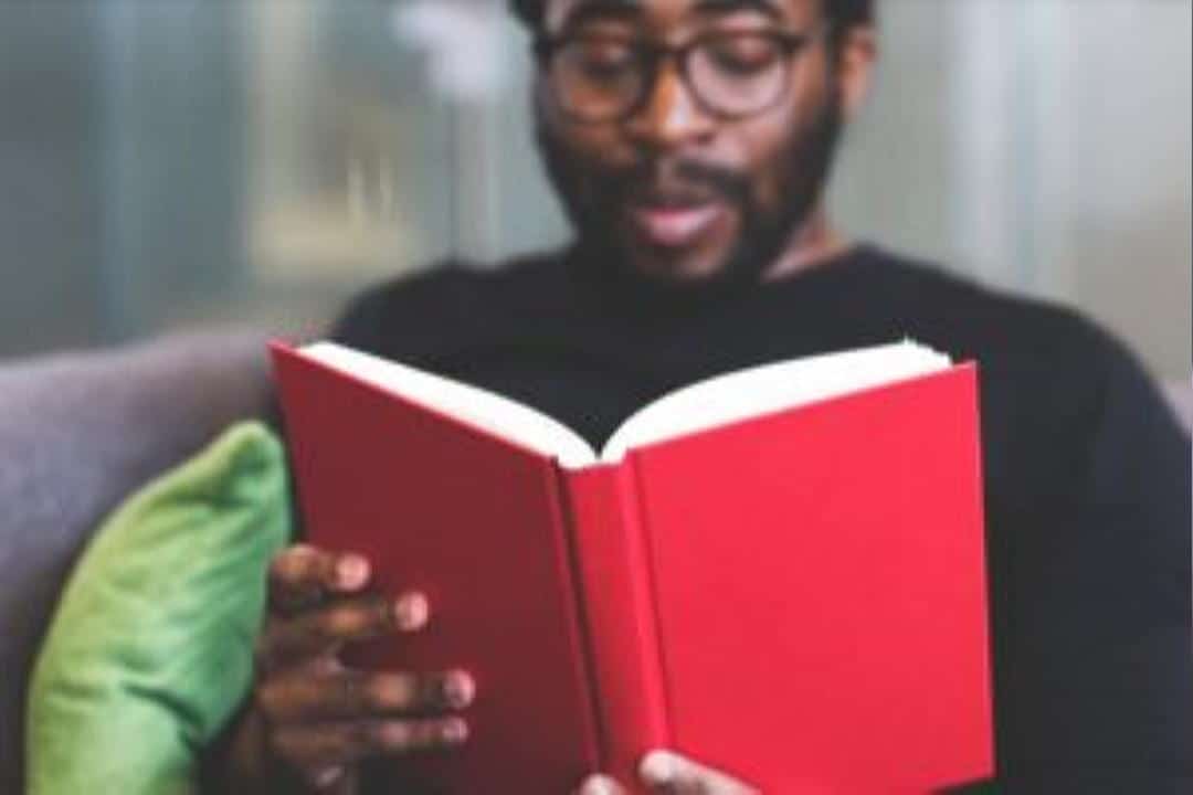 Man with glasses reading a red book.