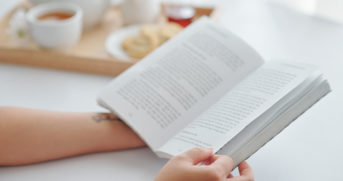 Close-up image of young woman having breakfast and reading book at home in the morning